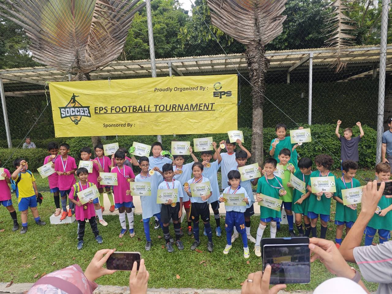 EPS players holding up medals and tournament certificates under the EPS Football Tournament banner